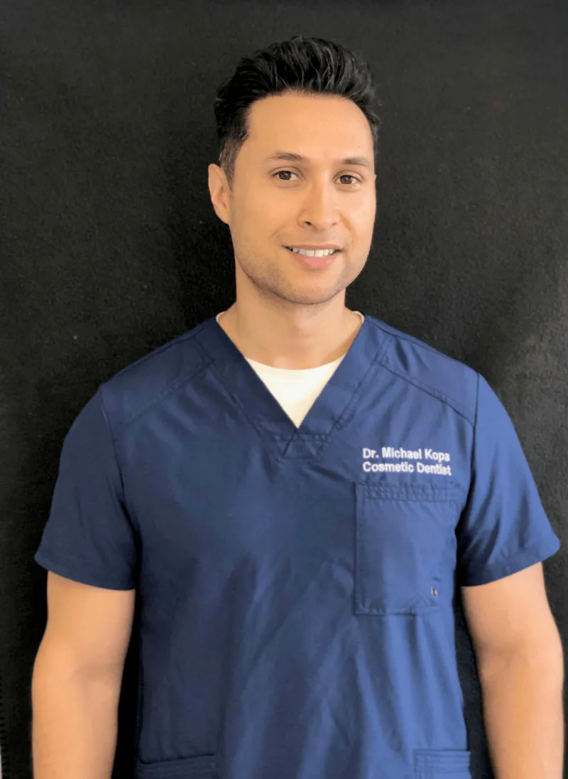 Smiling man wearing navy blue medical scrubs with text ‘Dr. Michael Kopa Cosmetic Dentist’ on pocket.