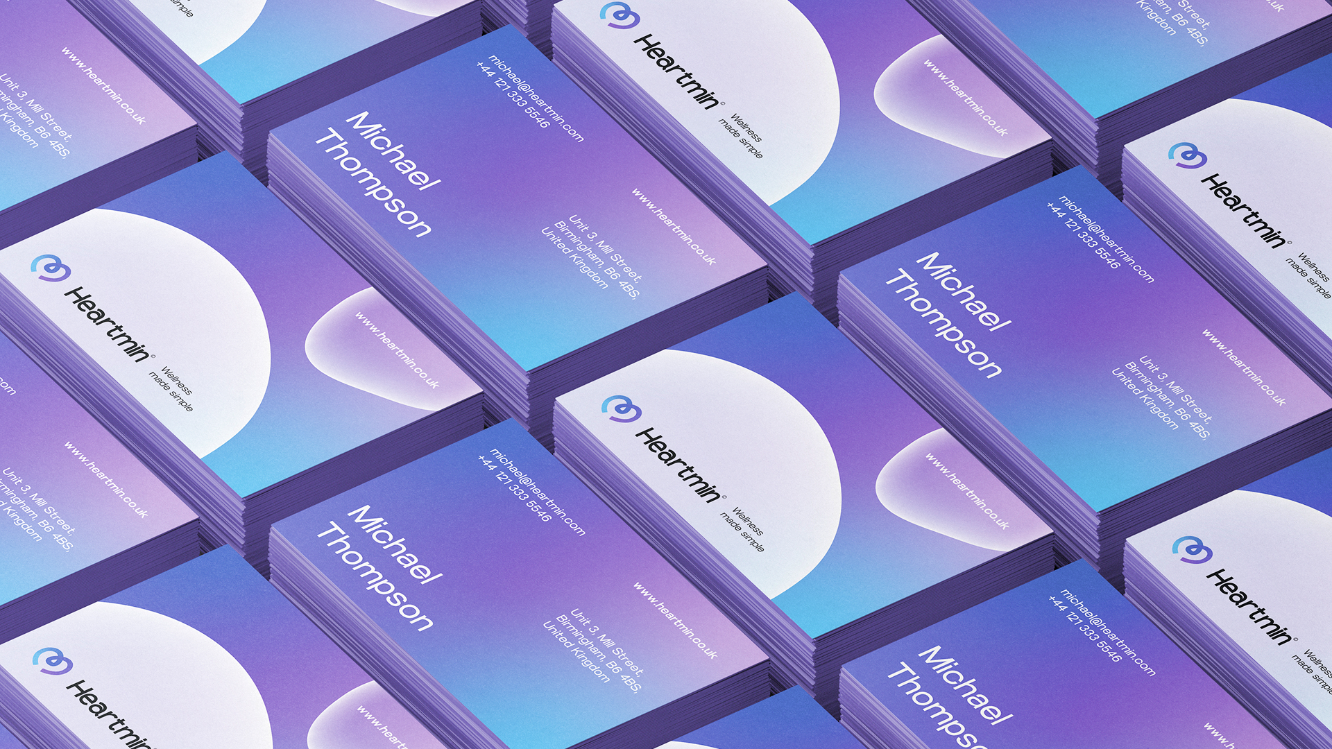 Stacks of purple and blue gradient business cards for Michael Thompson with Heartmin logo and contact details.
