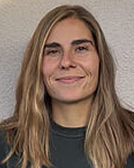 Porträt einer lächelnden Frau mit langen blonden Haaren vor einer grauen Wand.