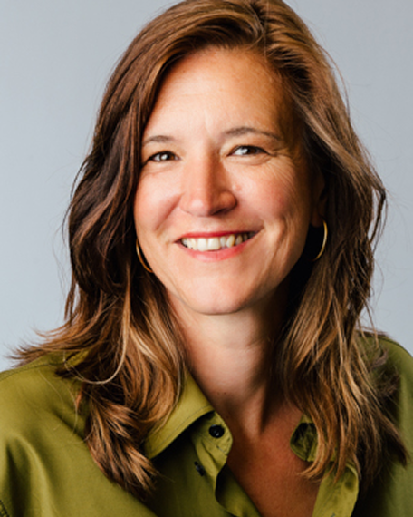 Lächelnde Frau mit schulterlangem braunem Haar und grüner Bluse vor grauem Hintergrund.