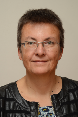 Porträt einer Frau mittleren Alters mit kurzer dunkler Frisur, die eine Brille und eine schwarze Lederjacke trägt.