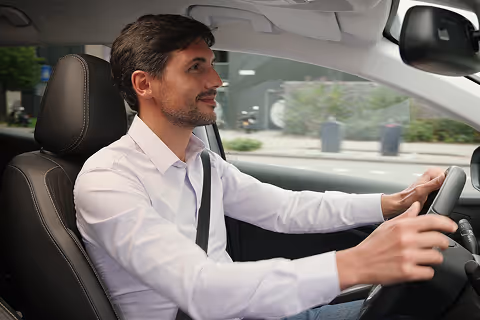 Man wearing a white shirt driving a car with a seatbelt fastened.