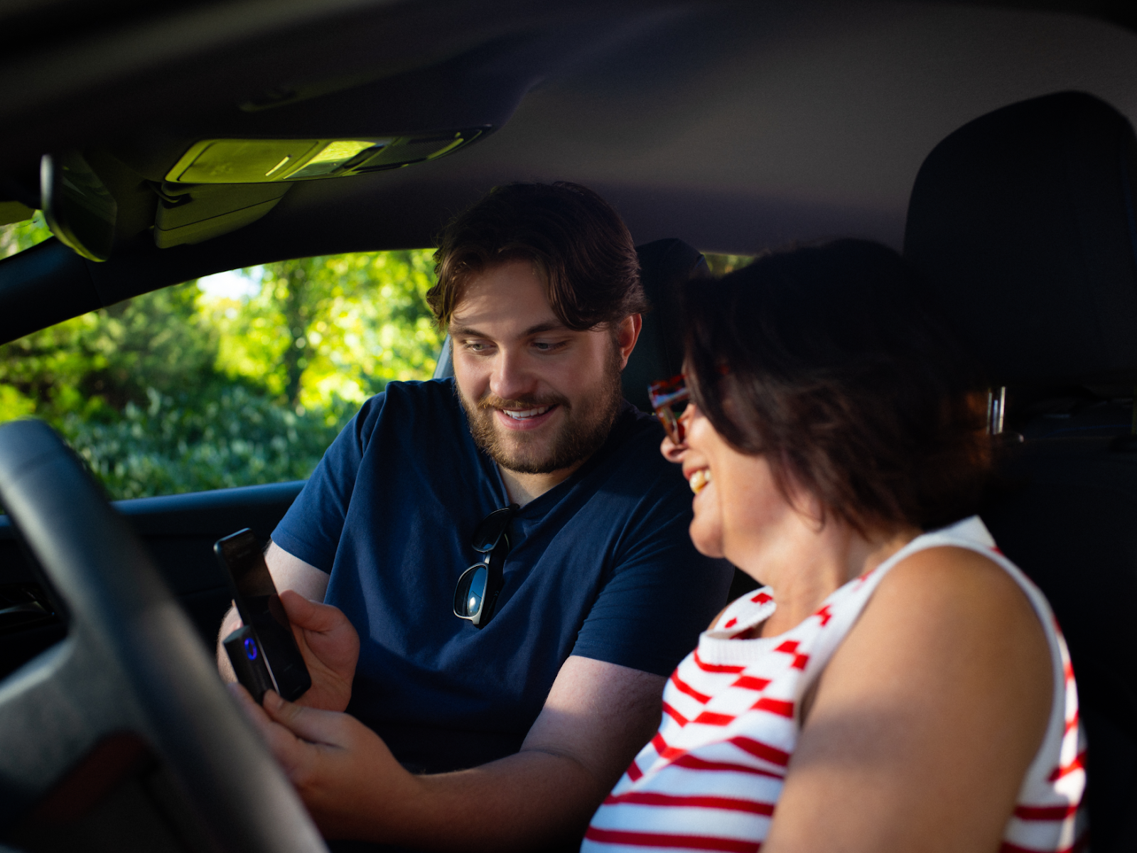 Person demonstrating AAWireless adapter and iPhone to another person in a car
