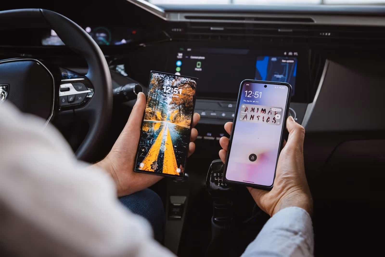 Two hands holding two phones in car in front of car dashboard