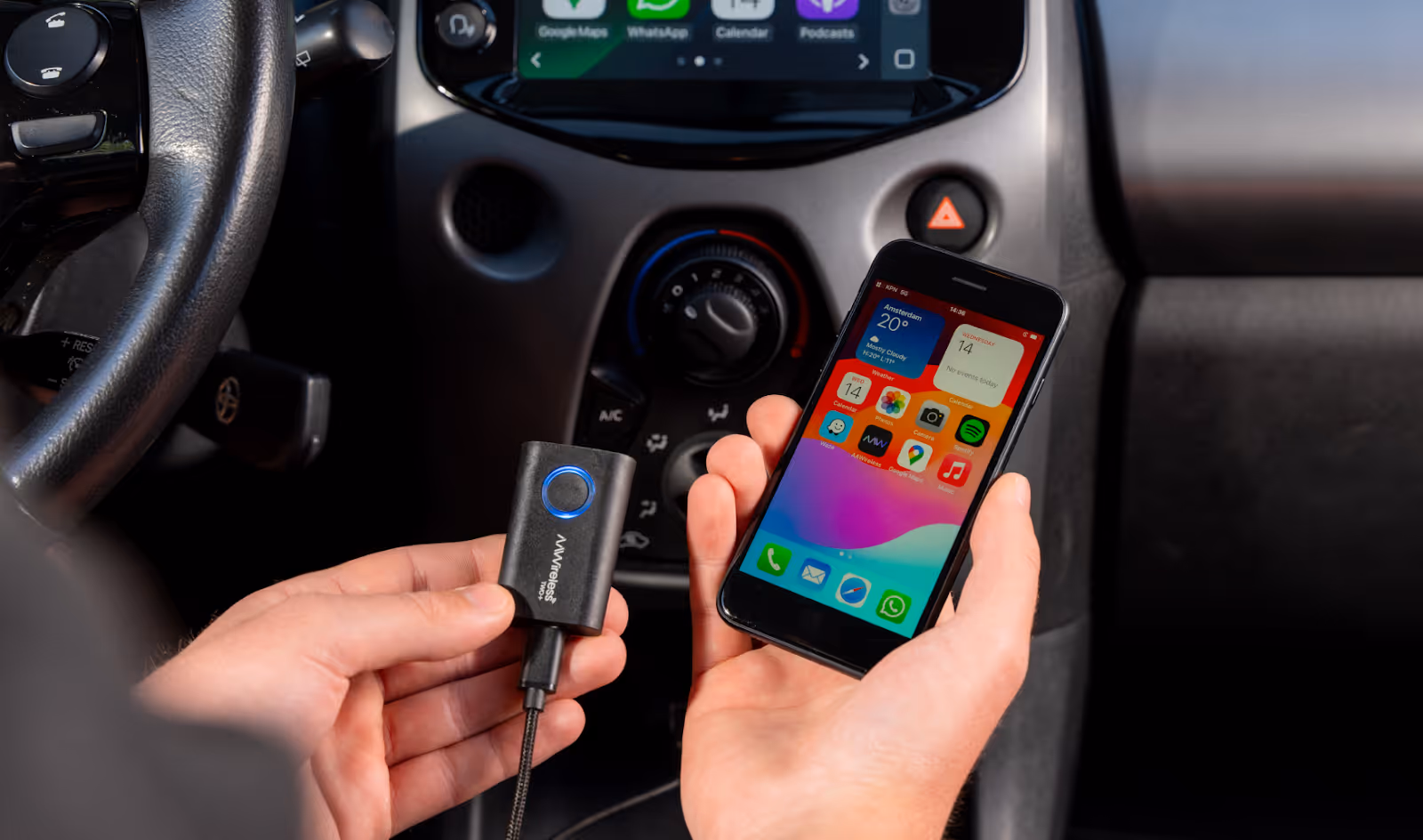 Hands holding an AAWireless TWO+ device and an iPhone in front of a car dashboard