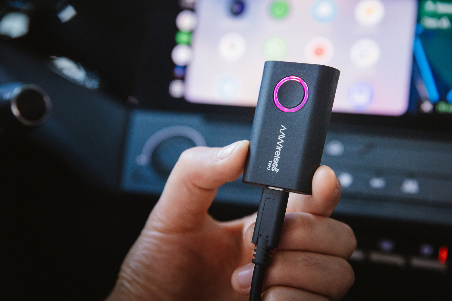 Hand holding an AAWireless dongle in front of a car dashboard.