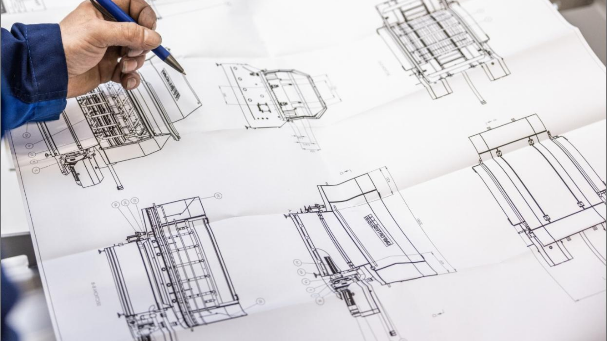 Hands holding a pen while reviewing complex paper engineering schematics.