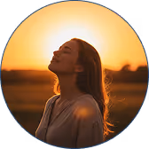Woman with closed eyes facing the sunset in a field during golden hour.