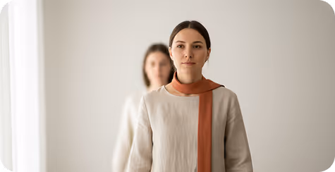 Calm woman with eyes closed sitting with arms wrapped around knees in a bright, minimalist room.