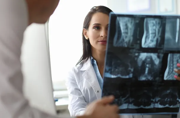 Female doctor examining spinal X-ray with a male patient in a medical office.