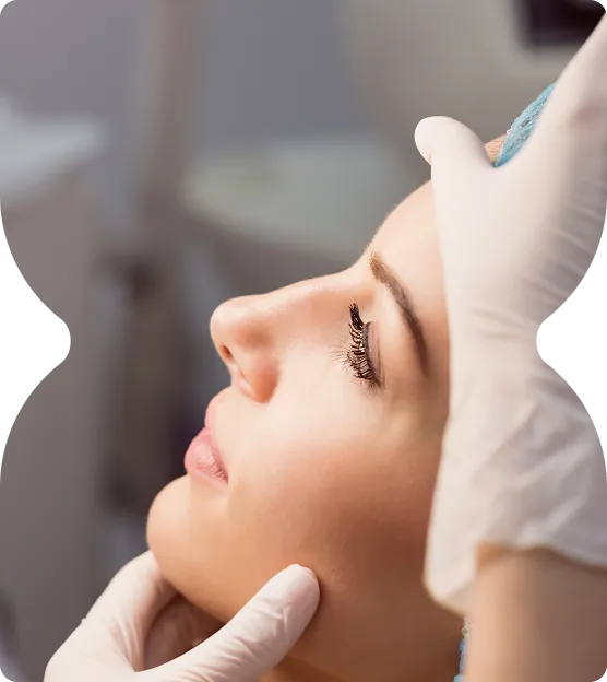 Close-up of a woman with closed eyes receiving a facial examination from a person wearing white medical gloves.