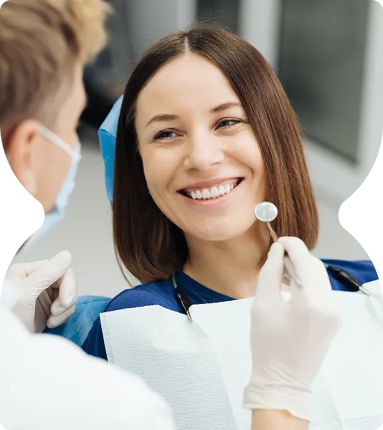Smiling woman sitting in dental chair while dentist holds dental mirror.