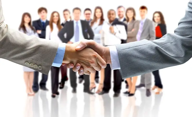 close up of 2 business men shaking each others hand with a group of business people blurred out in the background