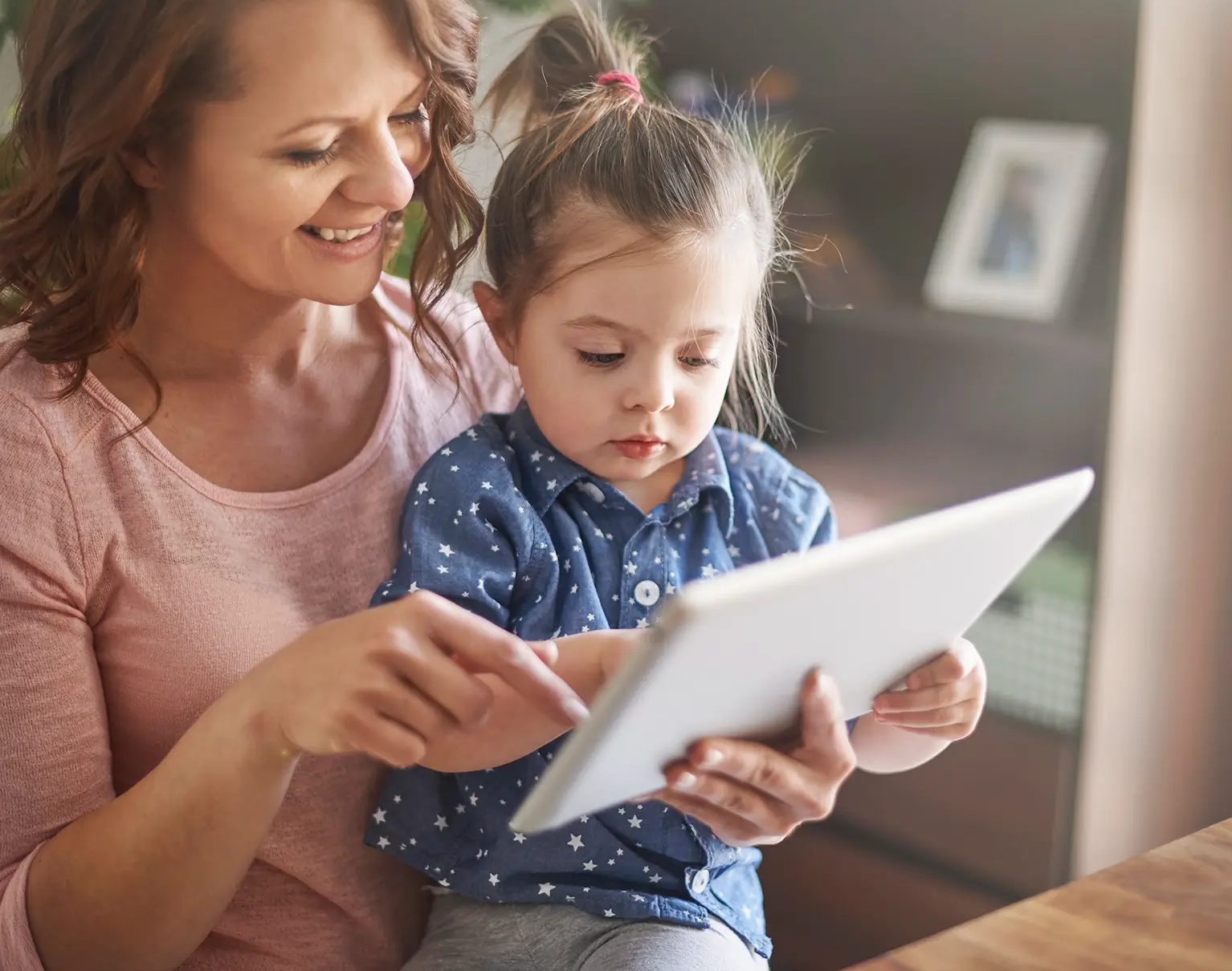 A smiling mum with her curious daughter reading on a tablet