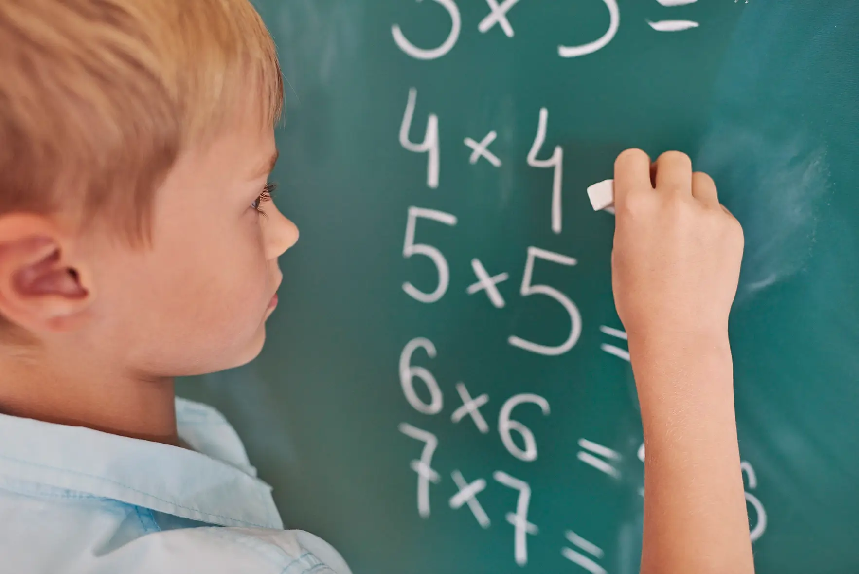 Boy doing timestables mathematical exercises on chalkboard
