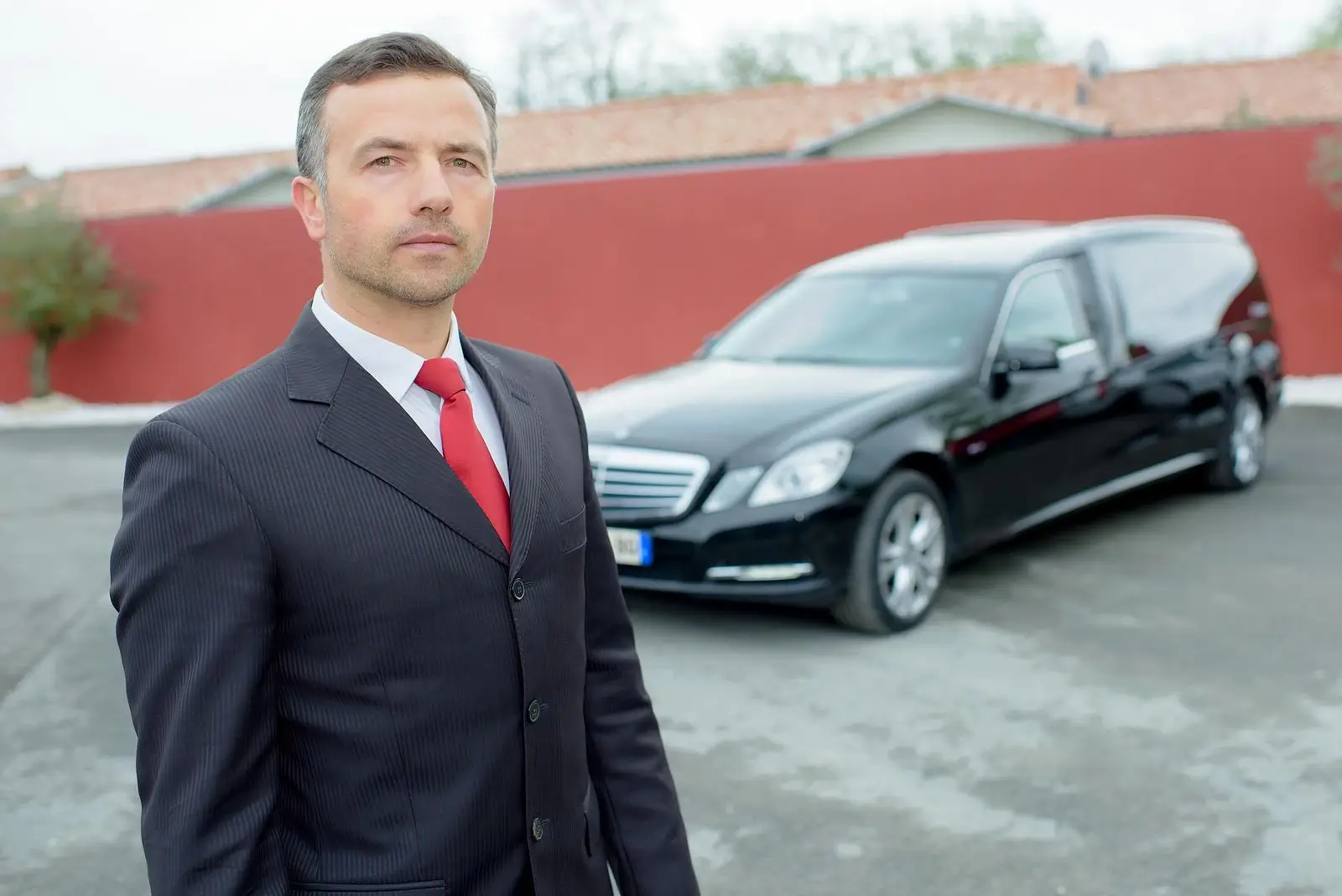 Face view of a funeral director with a black hearse in the background