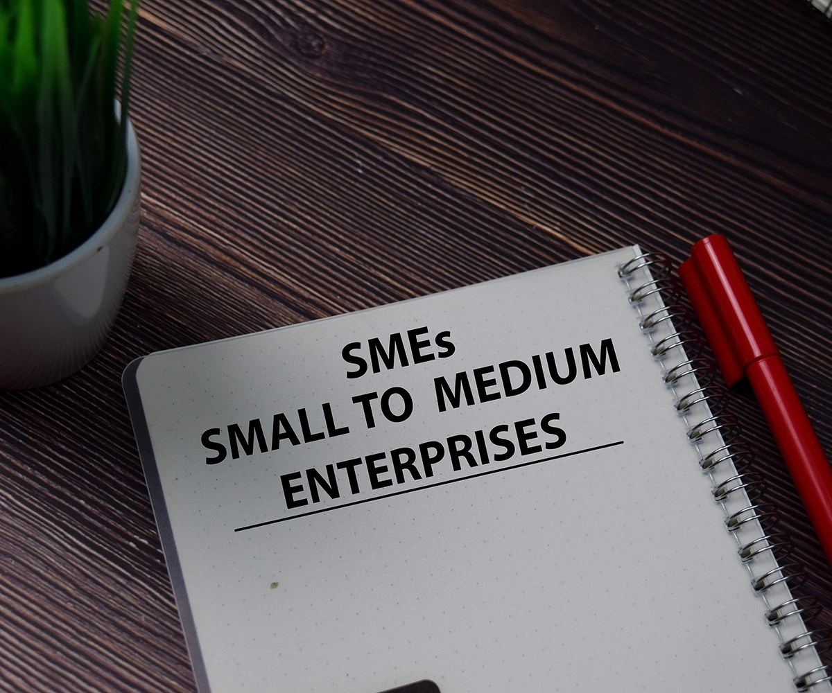 Close up of a plant pot, pen and a notepad on a desk with the text 'SMEs Small and medium Enterprises'