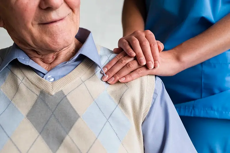 Close-up of a carer with there hand on the shoulder of a elderly man comforting them