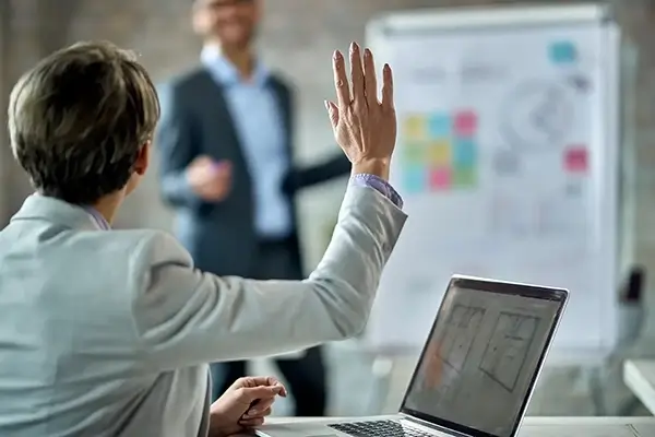 Close-up of a women in a meeting putting her hand up to ask a question
