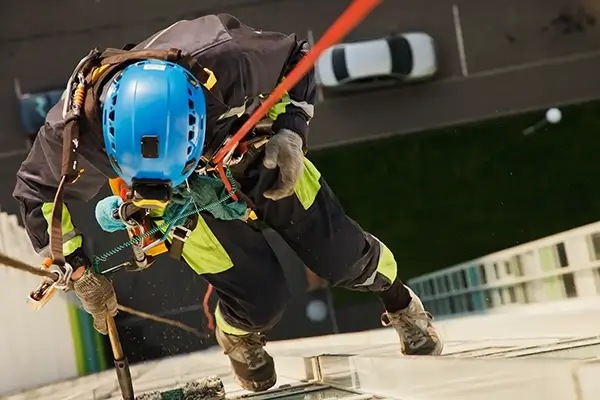 Worker abseiling from a building in full ppe kit including a rope harness, hardhat and full high-visibility jacket