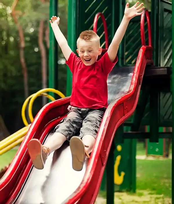 Young happy child sliding down a red slide in a playground
