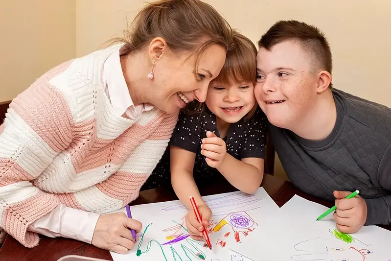 smiling women with two happy children with downs syndrome doing crafts