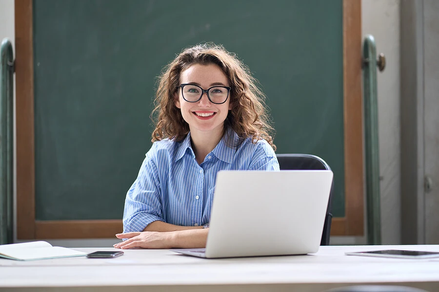 Teacher sits behind her text with an open laptop