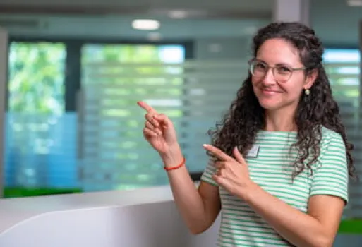 Frau mit Brille und lockigem Haar zeigt lächelnd mit beiden Händen nach links.