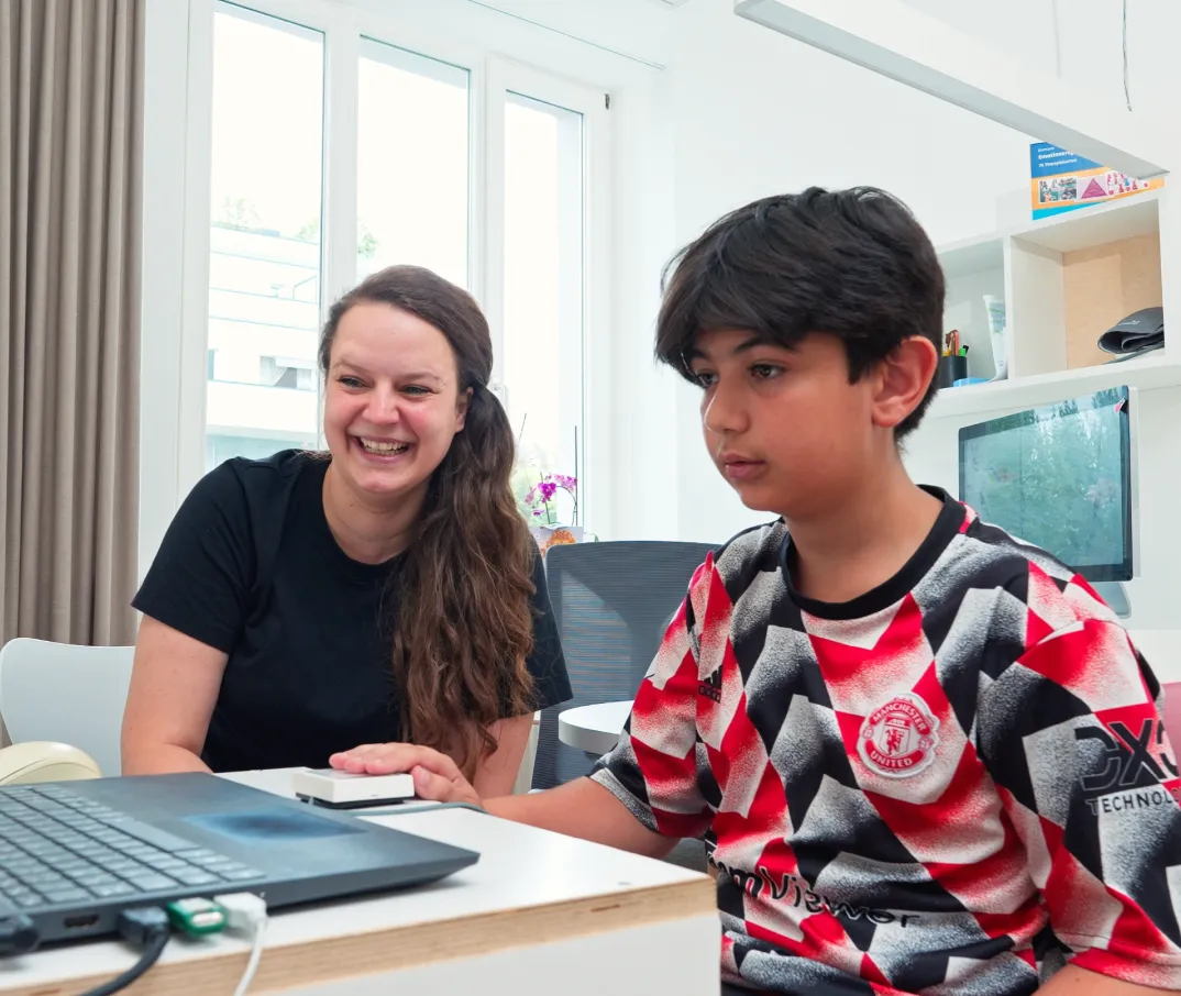 Ein Junge im Manchester United Trikot sitzt konzentriert vor einem Laptop, während eine lächelnde Frau neben ihm sitzt.