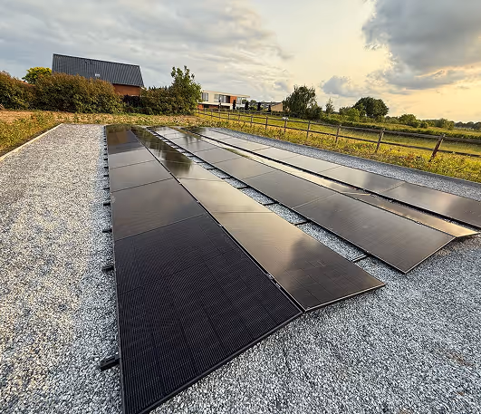 Dak met meerdere rijen zonnepanelen onder een bewolkte hemel bij een industrieel gebied.