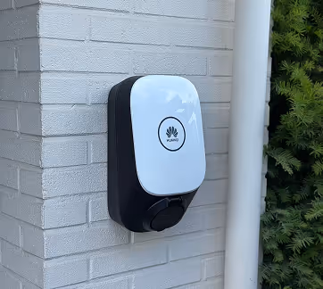 Huawei elektrische laadpaal bevestigd aan een witte stenen muur naast groene planten.