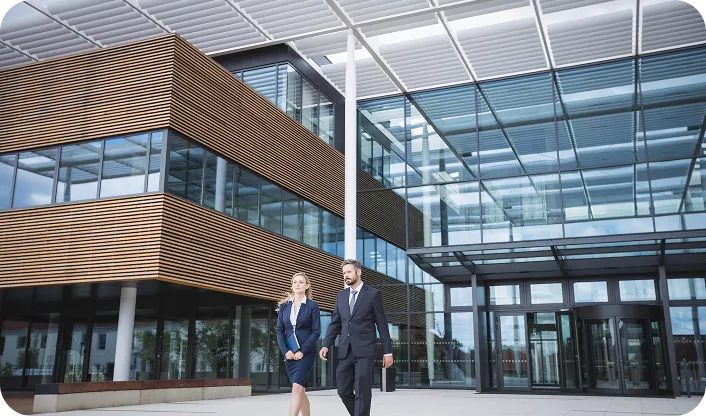 Two business professionals walking outside a modern glass and wood-clad office building.