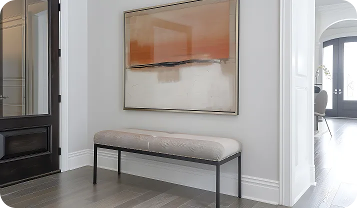 Modern hallway corner with a cushioned bench, abstract wall art, dark door on the left, and wooden flooring.