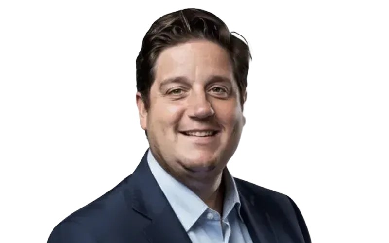 Smiling man with dark hair wearing a navy suit jacket and light blue shirt against a transparent background.