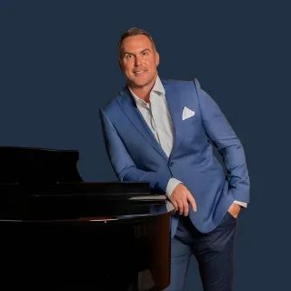 Smiling woman wearing glasses and a black hijab with a black blazer and striped shirt.