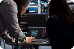 Two people working on a laptop displaying data visualization and code in a dimly lit office.