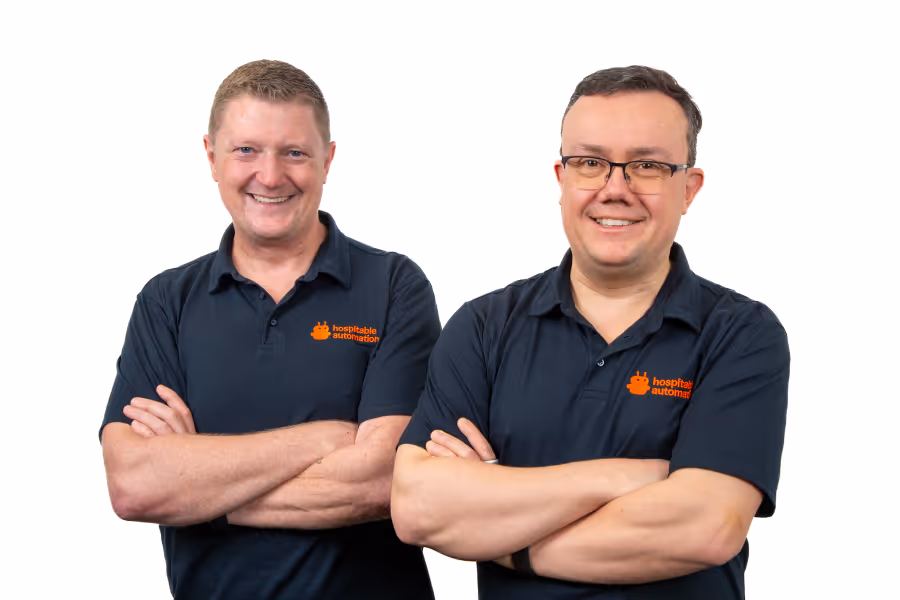 Two men standing side by side with arms crossed, wearing black polo shirts with orange hospitality automation logos, smiling against a white background.