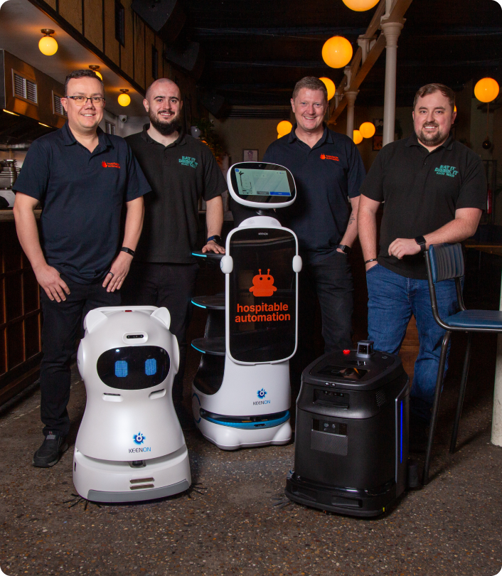 Four men standing indoors with three Keenon branded robots, one displaying the text 'hospitable automation'.