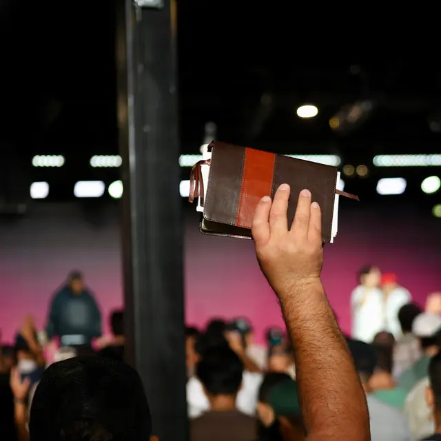 A hand raised holding a Bible during worship