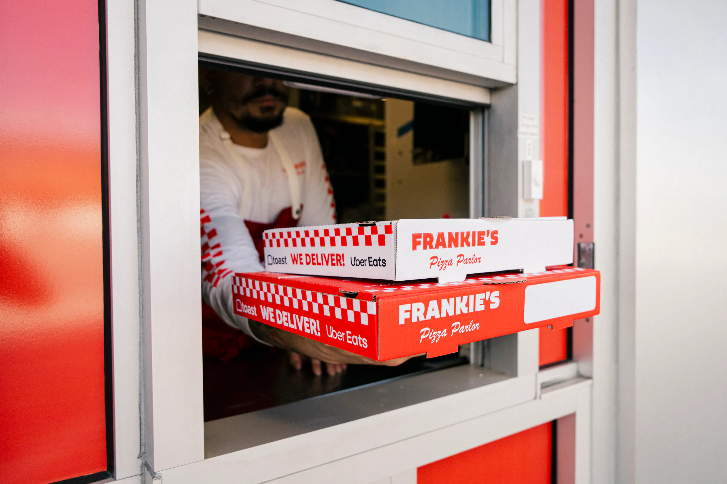 Frankie's Pizza Parlor staff handing pizza boxes through the delivery pickup window.