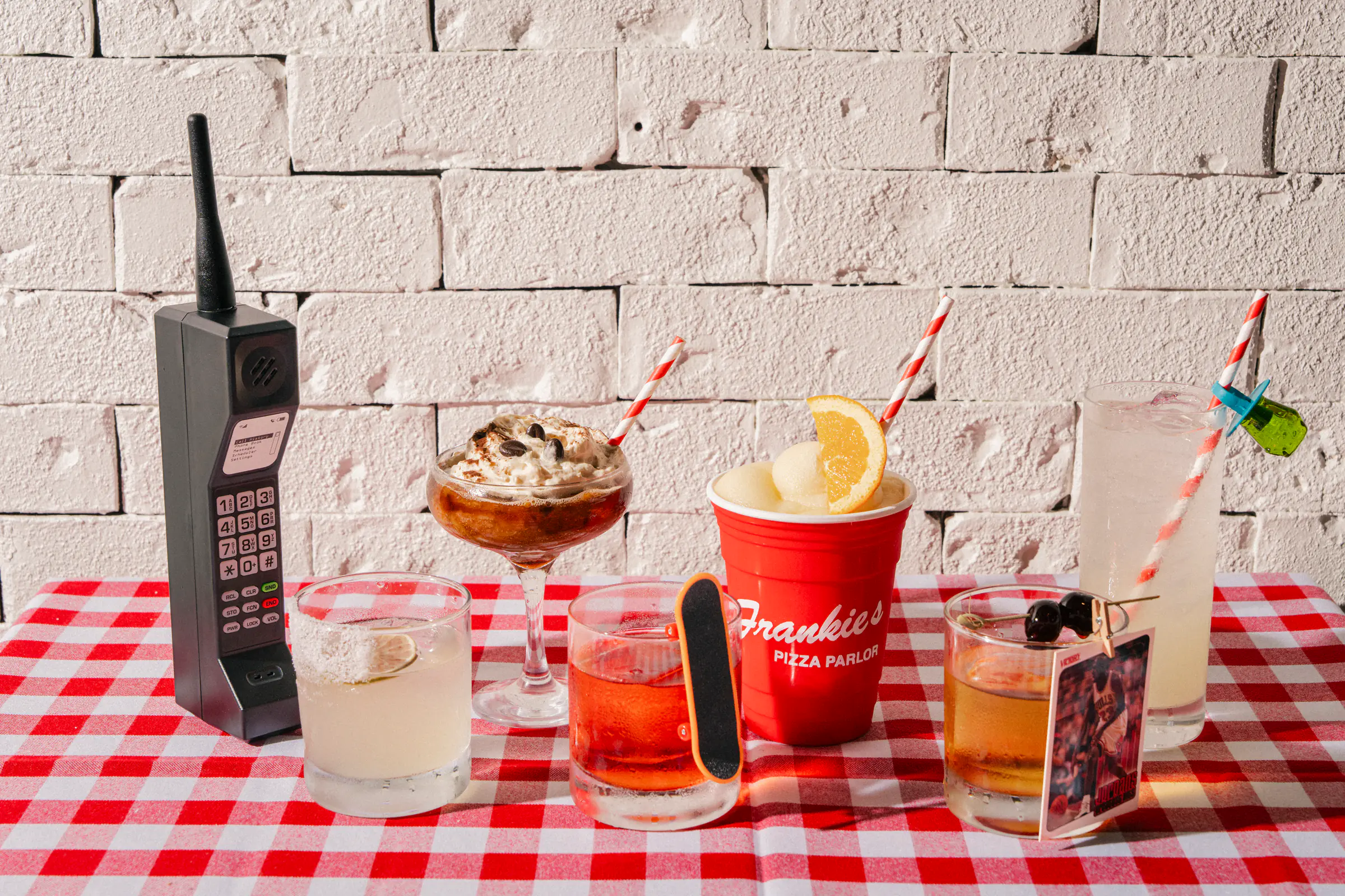 Assorted cocktails and a retro novelty phone on Frankie's Pizza Parlor's checkered tablecloth.