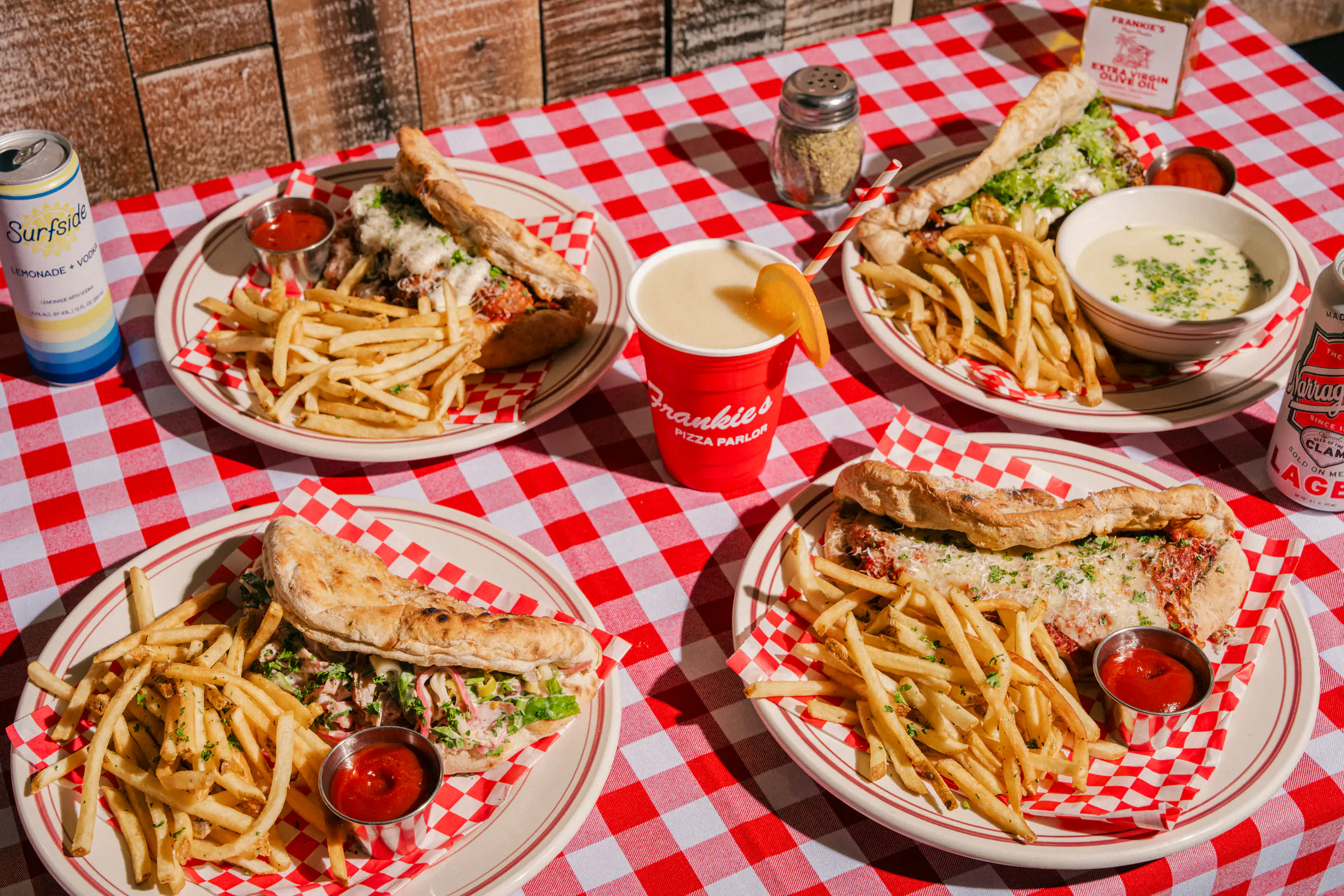 Sandwiches, fries, and drinks served on a red-checkered table at Frankie's Pizza Parlor.