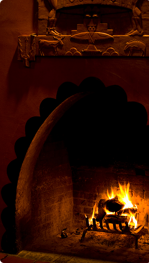 Lit wood-burning fireplace with arch-shaped brick opening and decorative adobe-style carving above.