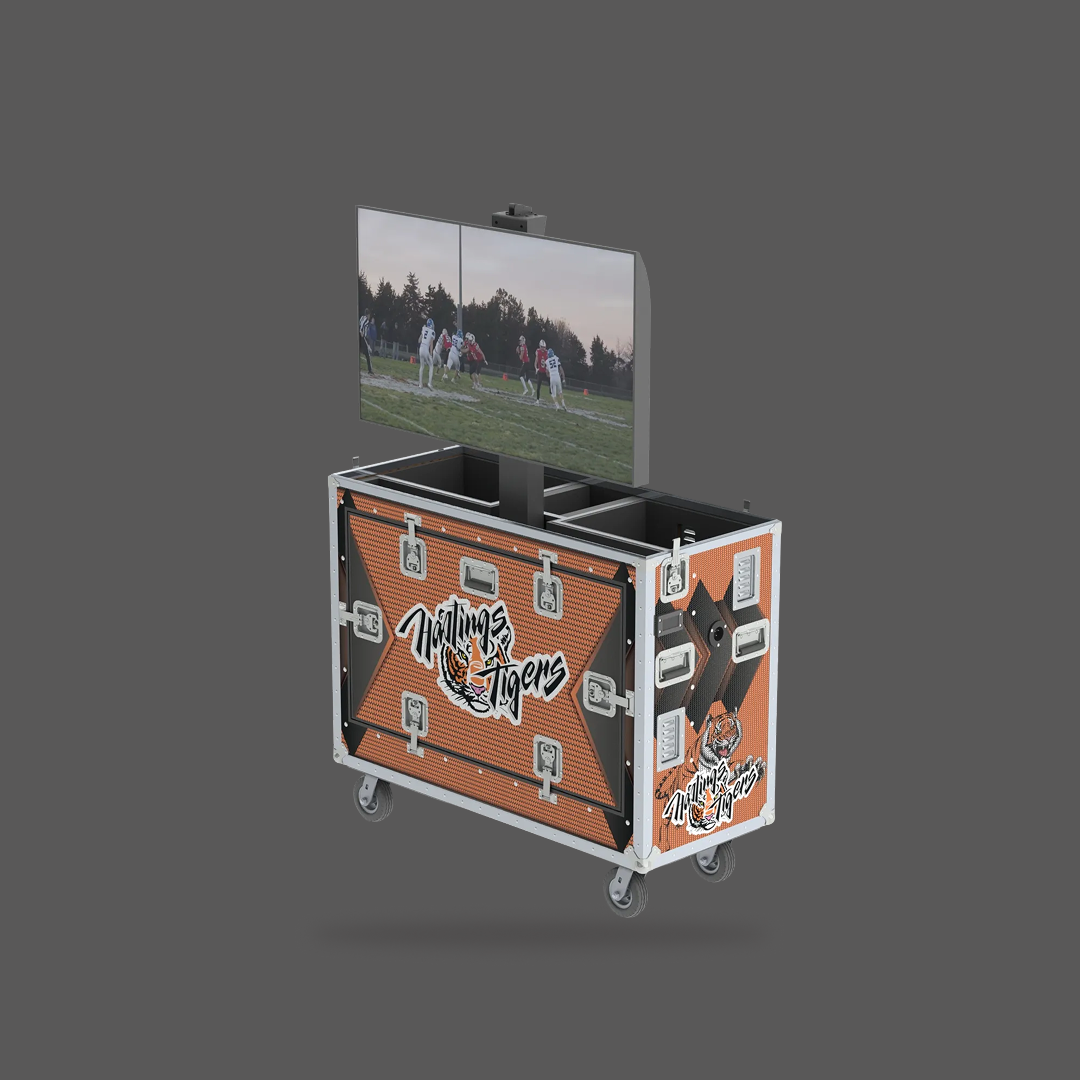 Hands holding a tablet showing instant replay video of a football game on a field with a crowd and cars in the background.