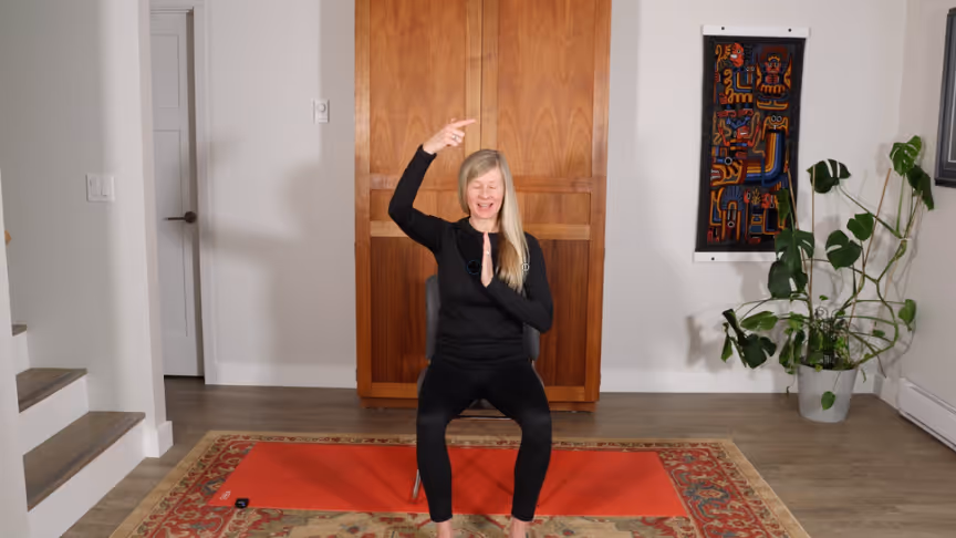Woman seated on a chair raising her arms during a lymphatic-support somatic practice