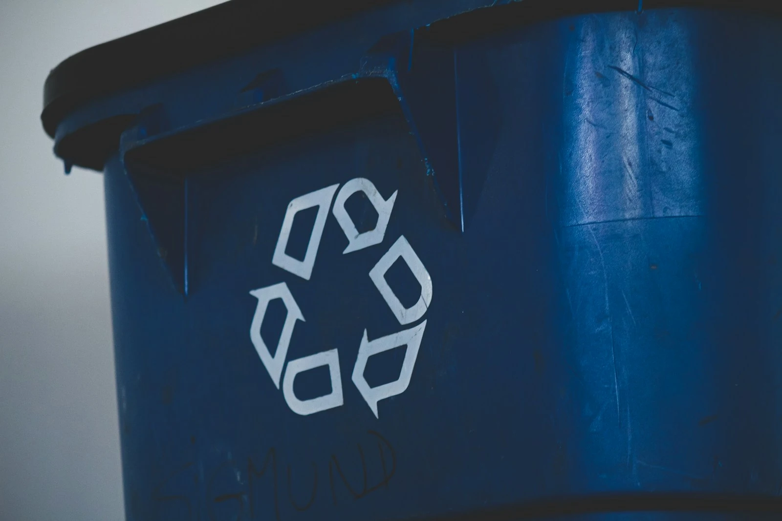 Close-up of a blue recycling bin featuring a white universal recycling symbol on its side