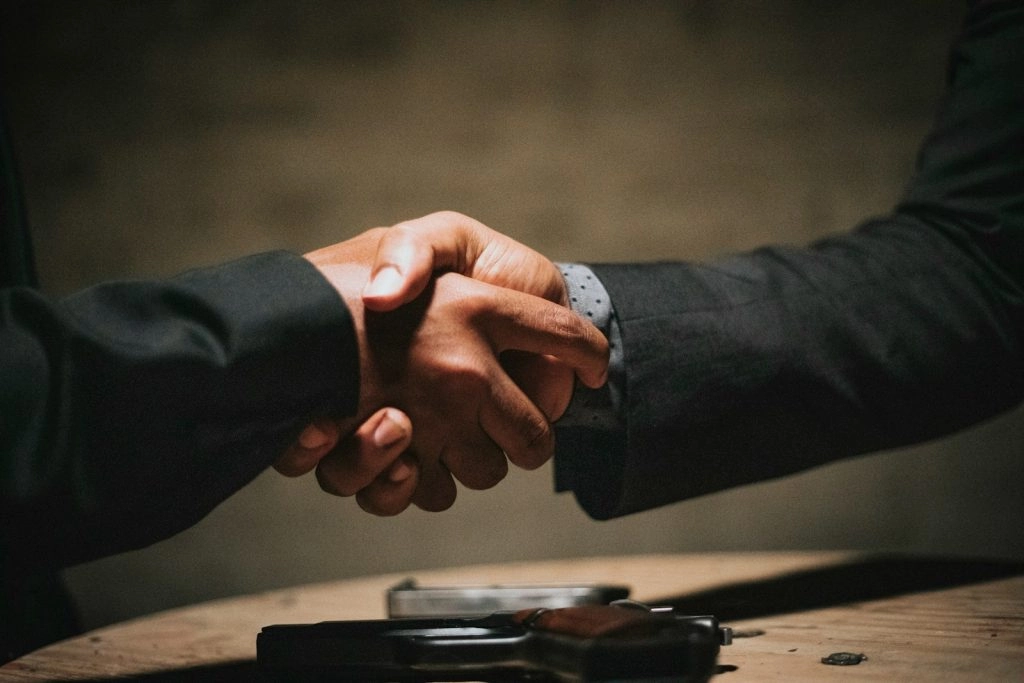 Close-up of a professional handshake over a wooden table, symbolizing a successful partnership or a won recruitment bid