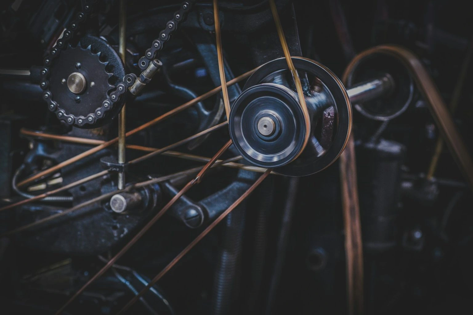 A close-up of intricate mechanical gears, chains, and spinning pulleys connected by several thin, taut belts in an industrial machine