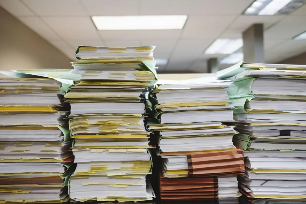 Close-up of massive piles of paperwork and files with yellow sticky tabs, symbolizing a heavy workload or complex bid management process