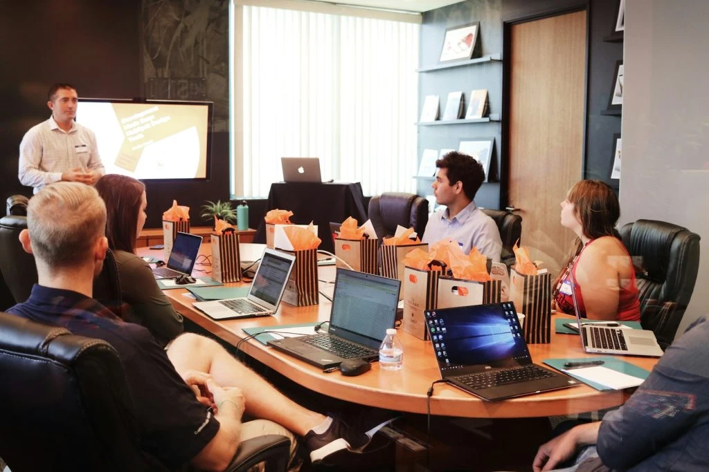 A professional business meeting with a team using laptops around a conference table during a presentation.